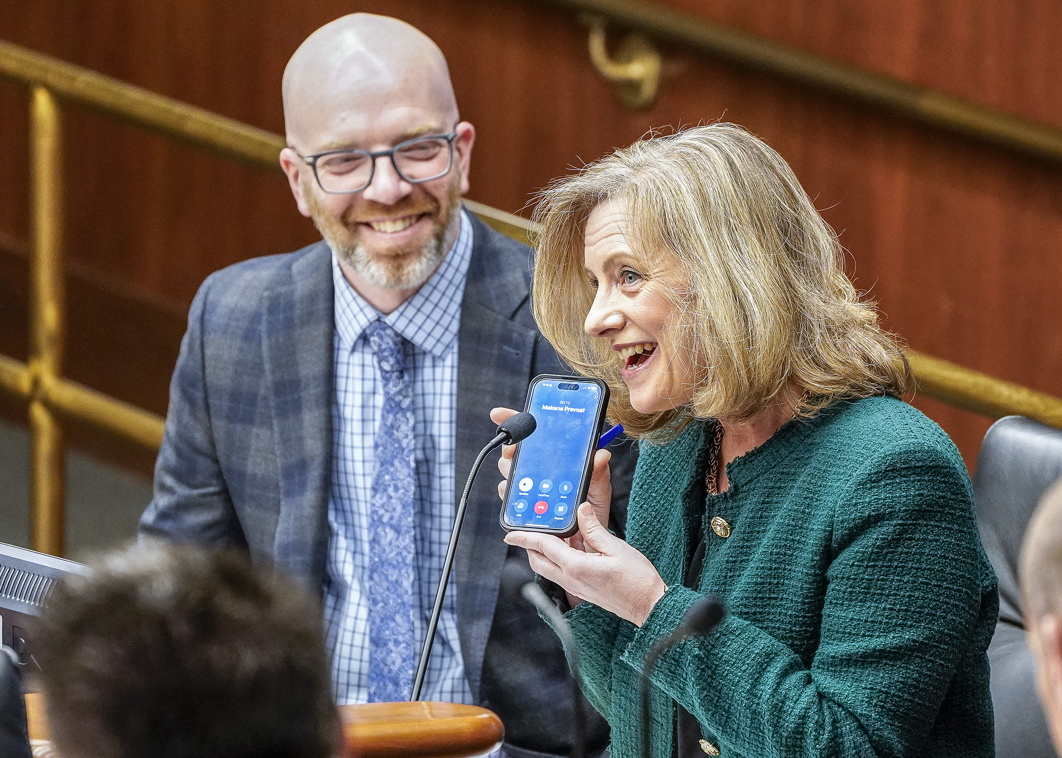 Rep. Kristin Robbins holds up her cell phone to allow Orono High School freshman Makena Prevost to testify remotely March 21 on an amendment to the transportation policy bill. Rep. Brad Tabke, left, sponsors the bill. (Photo by Andrew VonBank)